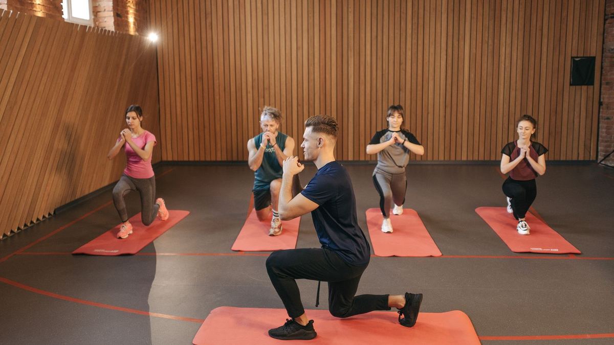 A fitness instructor leading a small class through a lunge on red mats
